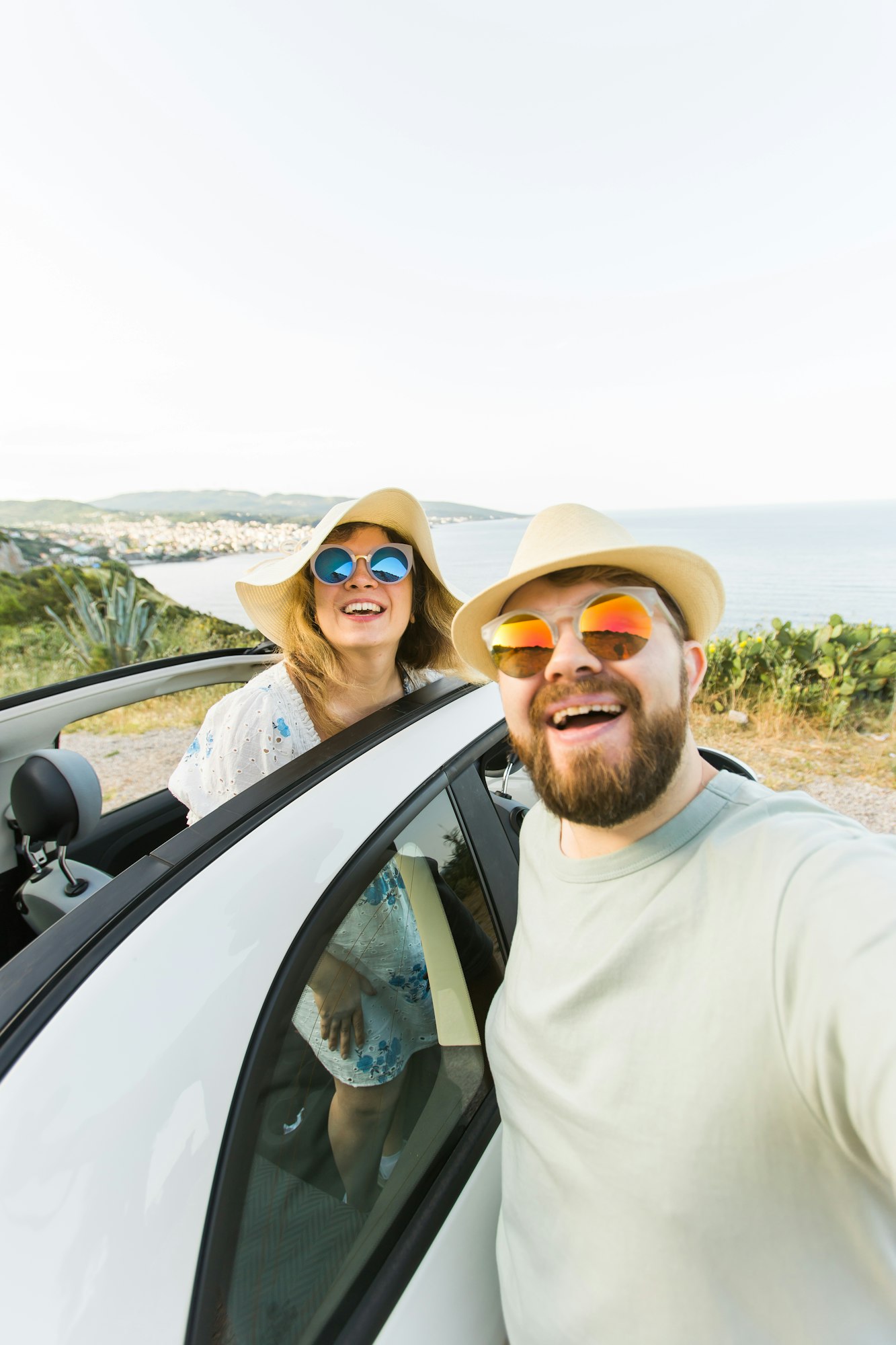 Romantic couple making selfie on smartphone camera in rental cabrio car on ocean or sea beach